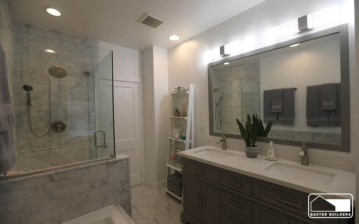 Marble shower with glass enclosure beside a gray double vanity