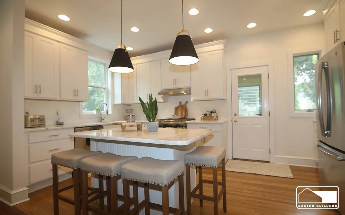 White kitchen with black drum pendants over a marble-topped island